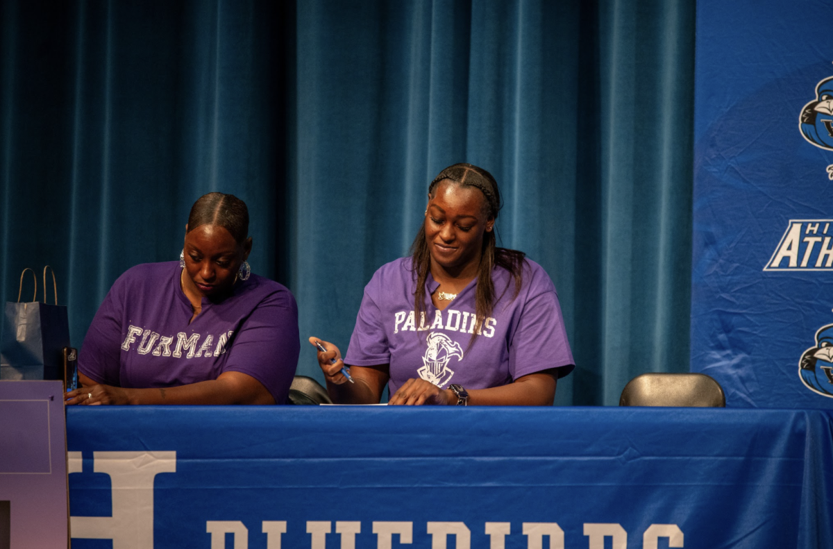 Ty Berry (12) puts pen to paper as she makes her commitment to Furman University to play basketball official. 